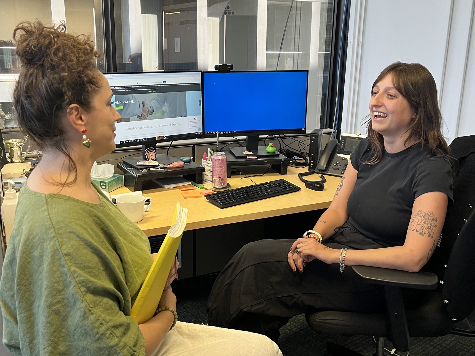 Two members of the IMA Solutions coordination team chatting at a desk